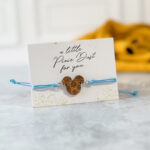 Blue string bracelet with engraved wooden mouse-shaped charm on a card that reads “a little Pixie Dust for you”