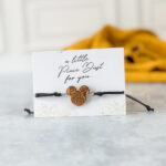Black cord bracelet with engraved wooden mouse-shaped charm on a card that says “a little Pixie Dust for you”