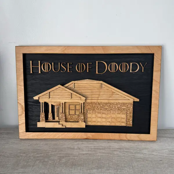 Wood-framed black chalkboard sign reading 'House of Doody' with a wooden house illustration plate beneath.