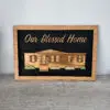 Wood-framed chalkboard showing the phrase 'Our Blessed Home' with a wooden house illustration beneath it.