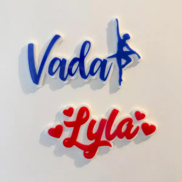 Two acrylic name magnets reading Vada and Lyla in blue and red script with dancer silhouette and heart accents